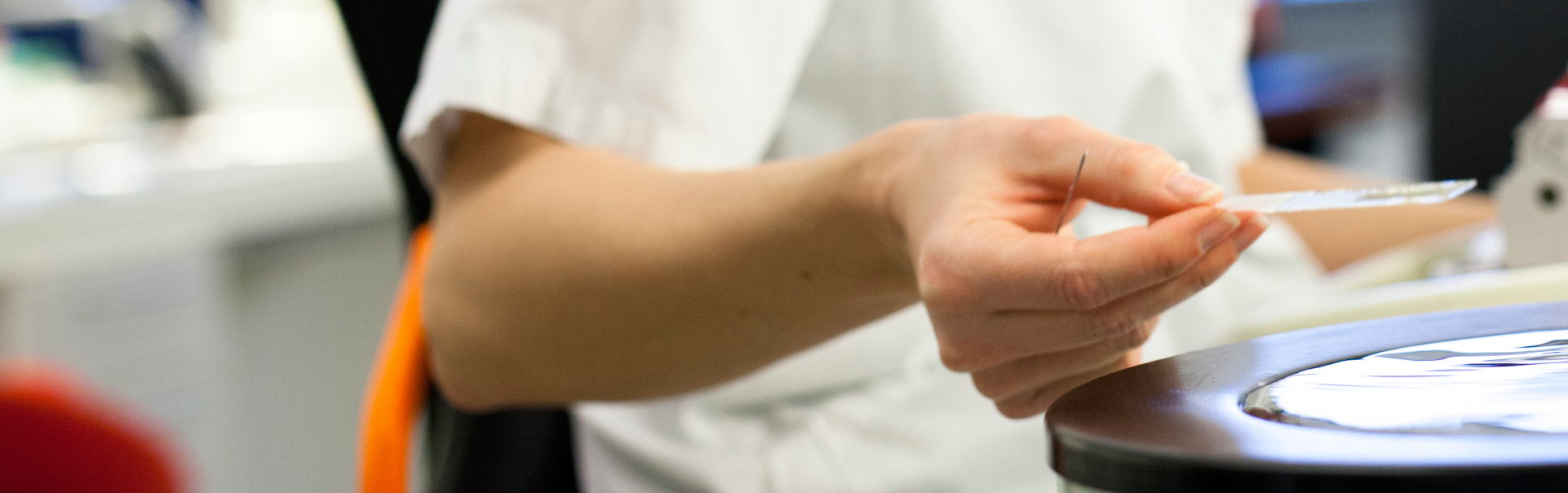 En person i hvit labfrakk jobber med en Leica RM maskin, holder en tynn glassplate i et laboratorium