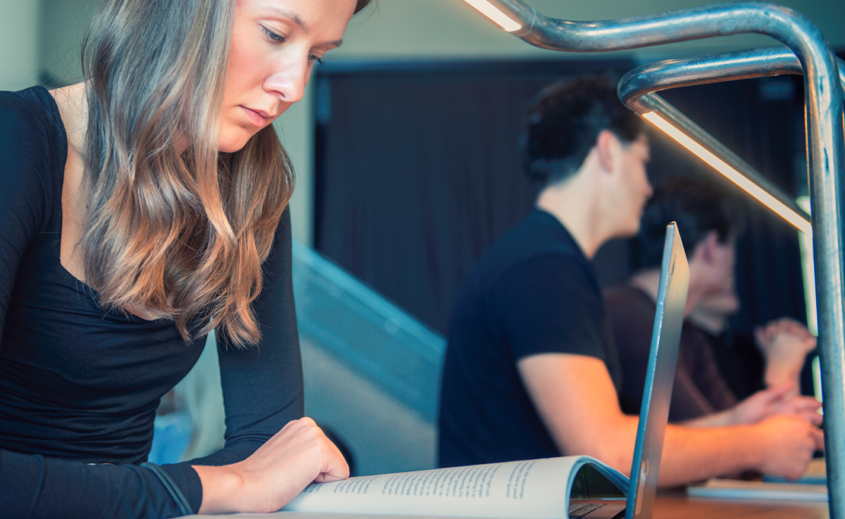 The picture shows a young woman with long hair studying in a reading room.