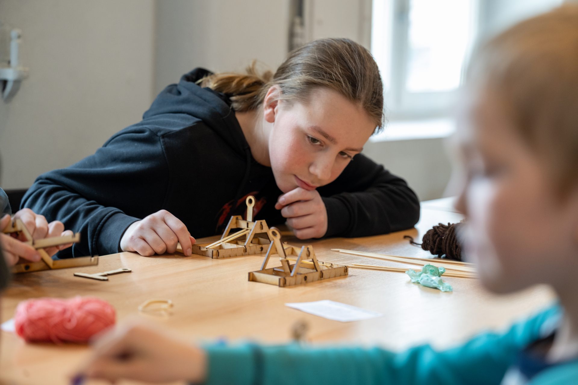En jente lener seg over en pult og studerer katapulten hun har bygget. Rundt henne bygger barn egne oppfinnelser.