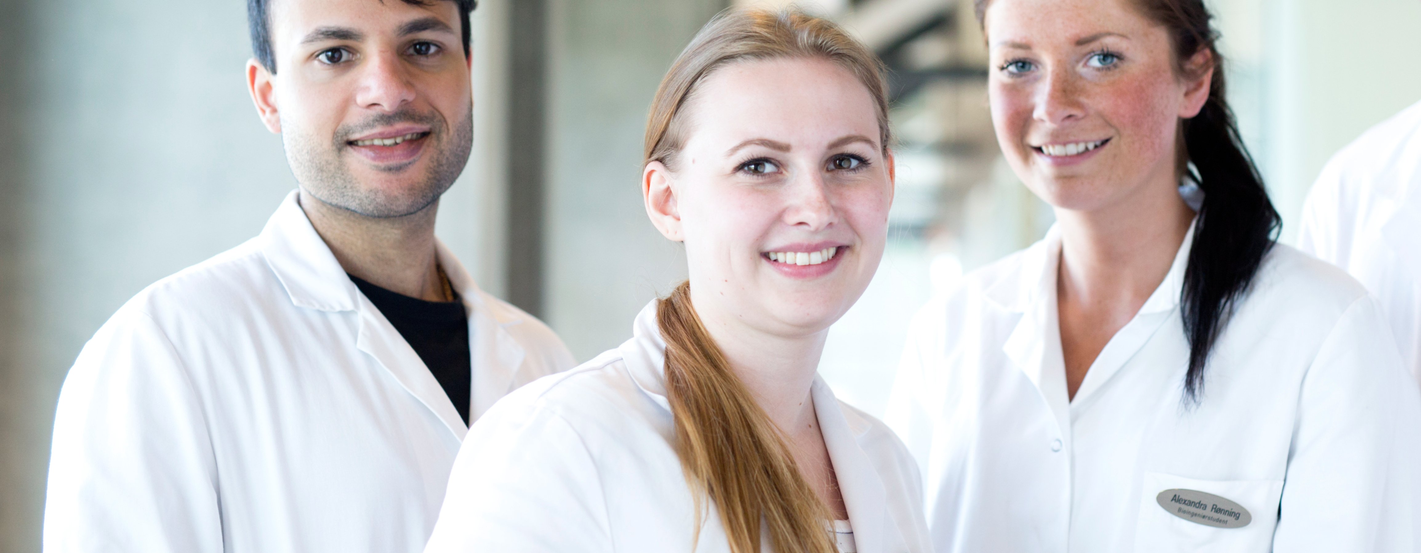 Three people in white lab coats stand together in a modern, indoor laboratory environment.