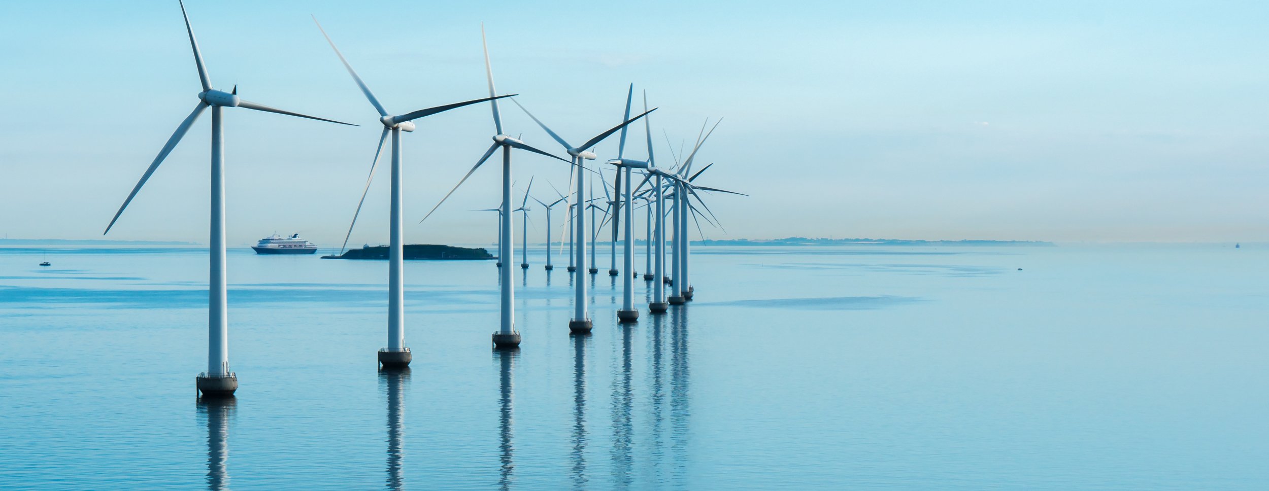 The picture shows several windmills in the sea under a bright blue sky, with a ship in the background.