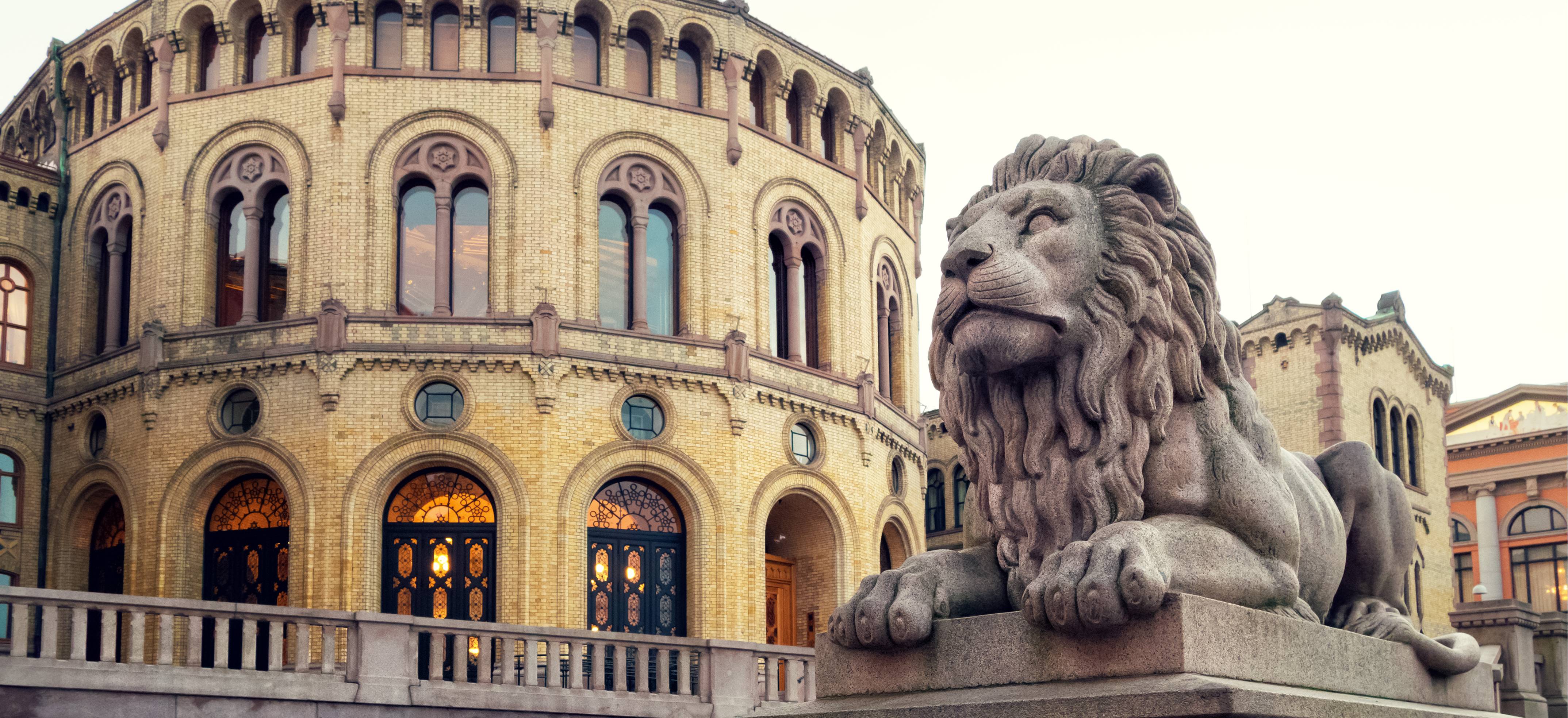 The picture shows the Storting building in Oslo with a lion statue in the foreground