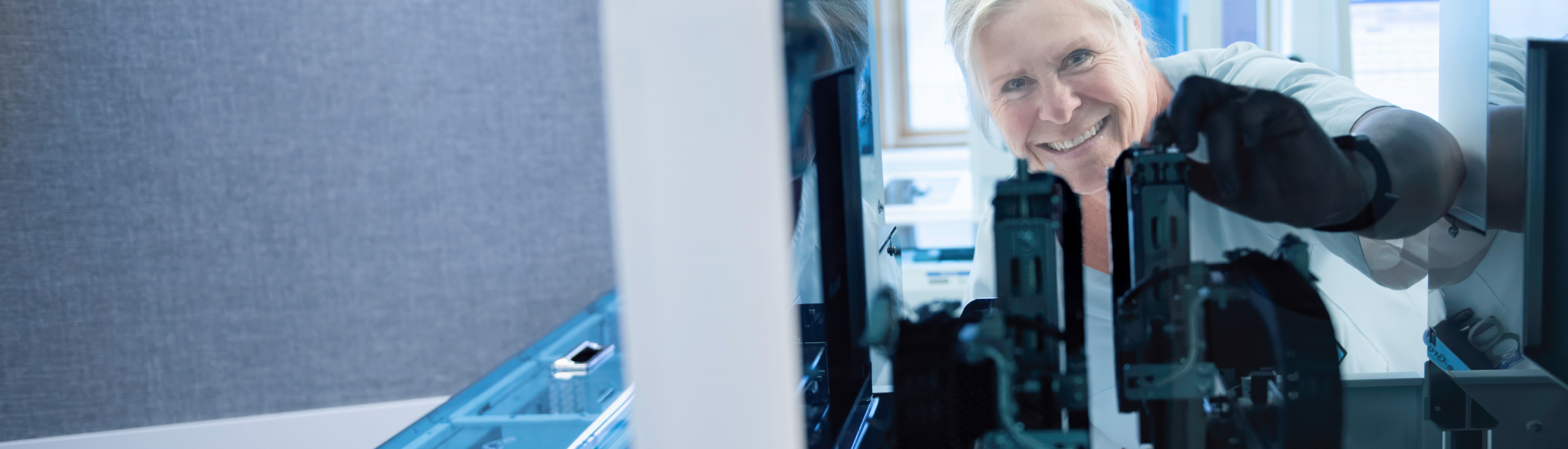 A smiling bioengineer in a white coat works with advanced technical equipment in sterile surroundings inside a modern laboratory. Photo: Luca Kleve-Ruud.