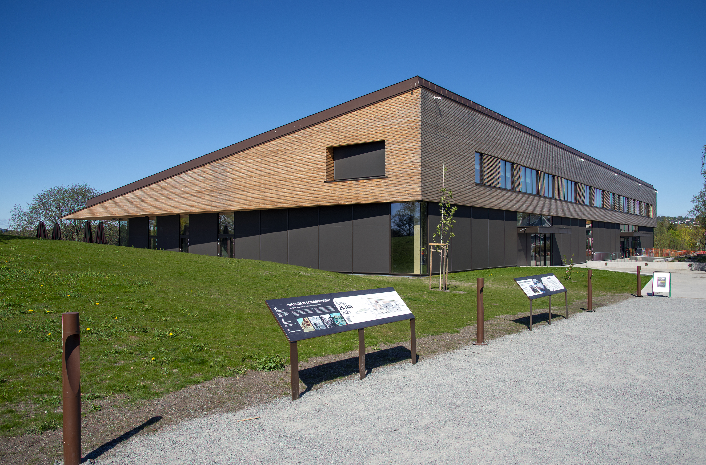 Bilde av det nye regionale historiesenteret på Domkirkeodden med skilt i forgrunnen. Lavt trehus med vinduer. Bildet er tatt mot et hjørne av huset. Kredit: Geir Ove Andreassen, Anno Domkirkeodden historiesenter