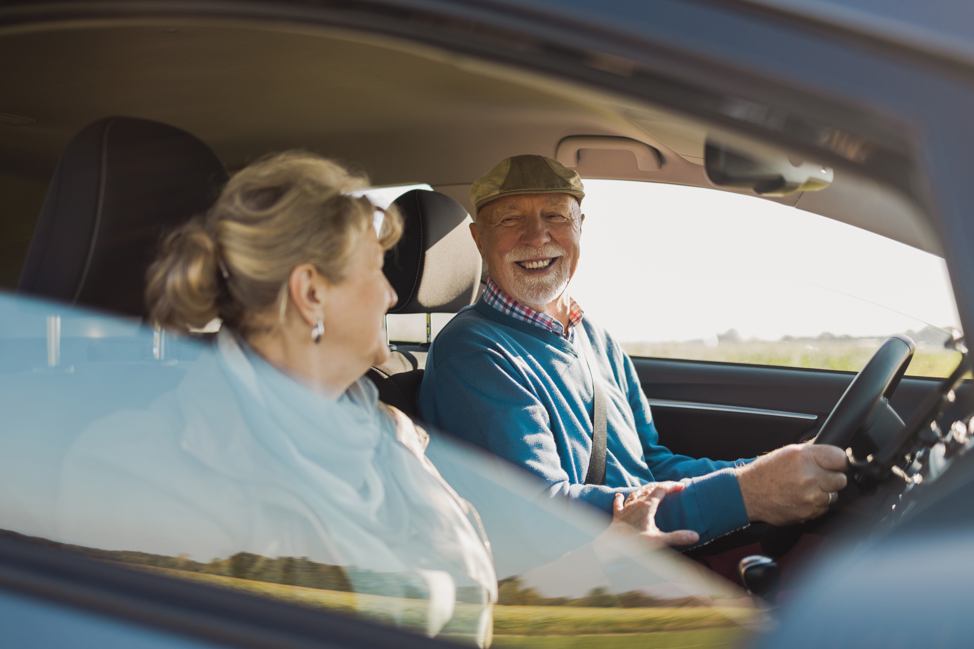 A smiling elderly couple drives a car, symbolizing security and a positive future that can be secured through good collective agreements and working conditions.