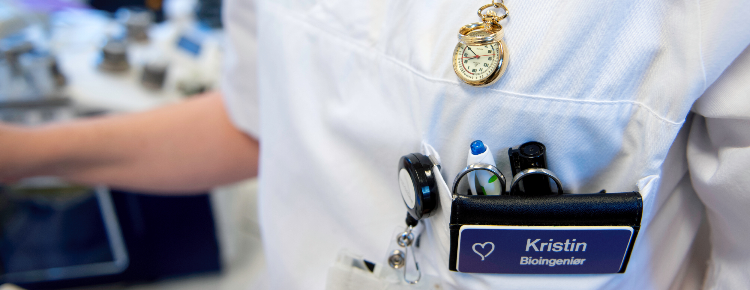 A bioengineer in a white uniform with a name tag, watch and work tools visible in his pocket, ready to work in the laboratory.
