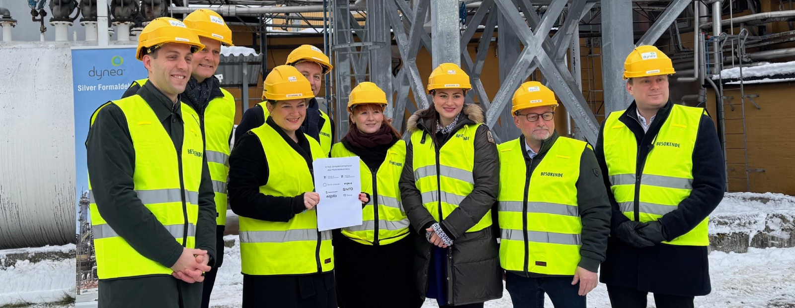 Bildet viser åtte personer i hjelmer og refleksvester under en avtalesignering med fokus på industri og bærekraft.