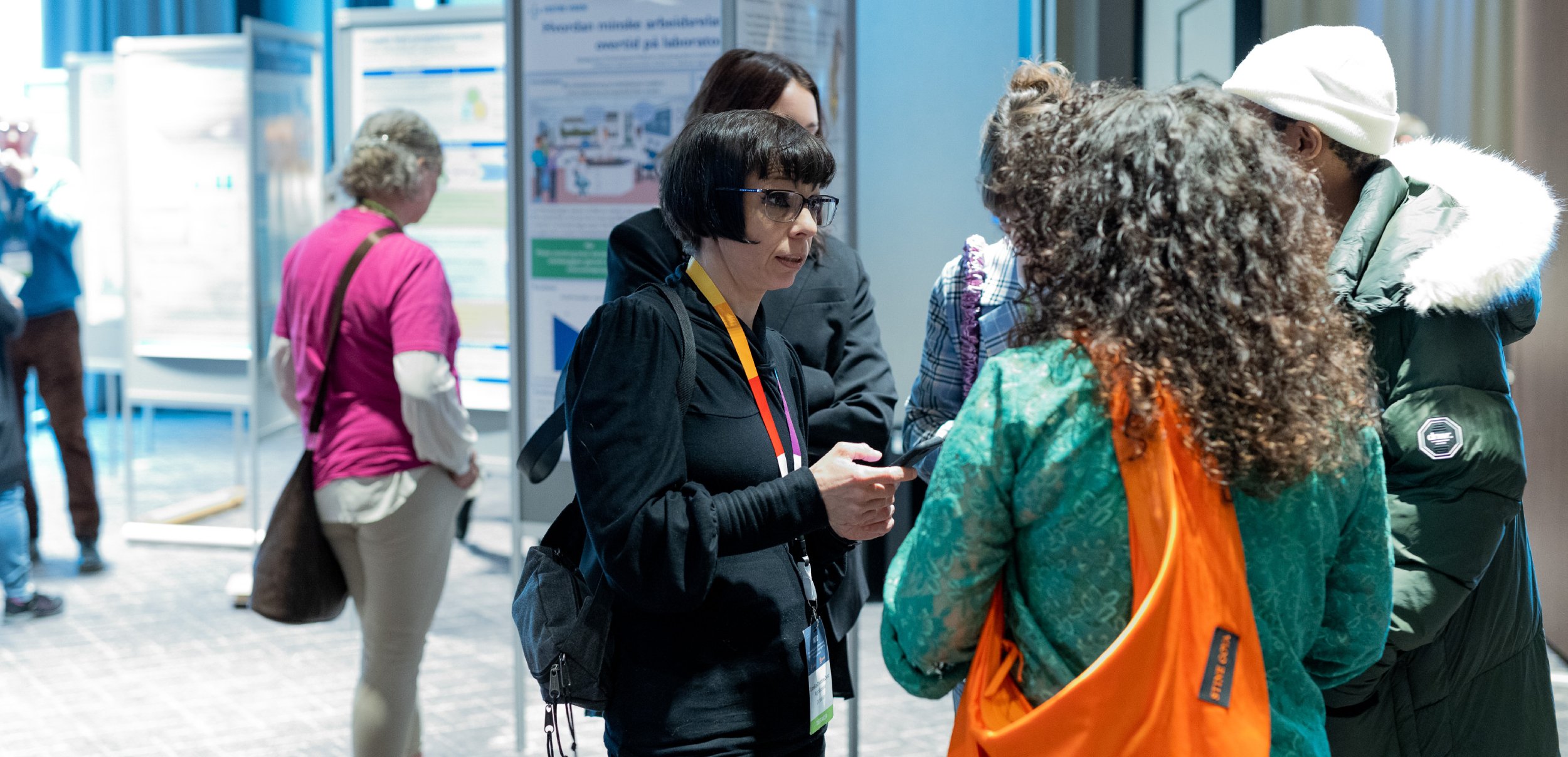 The picture shows a group of people standing in a room with several posters. The posters contain information, diagrams and illustrations that are part of an exhibition.