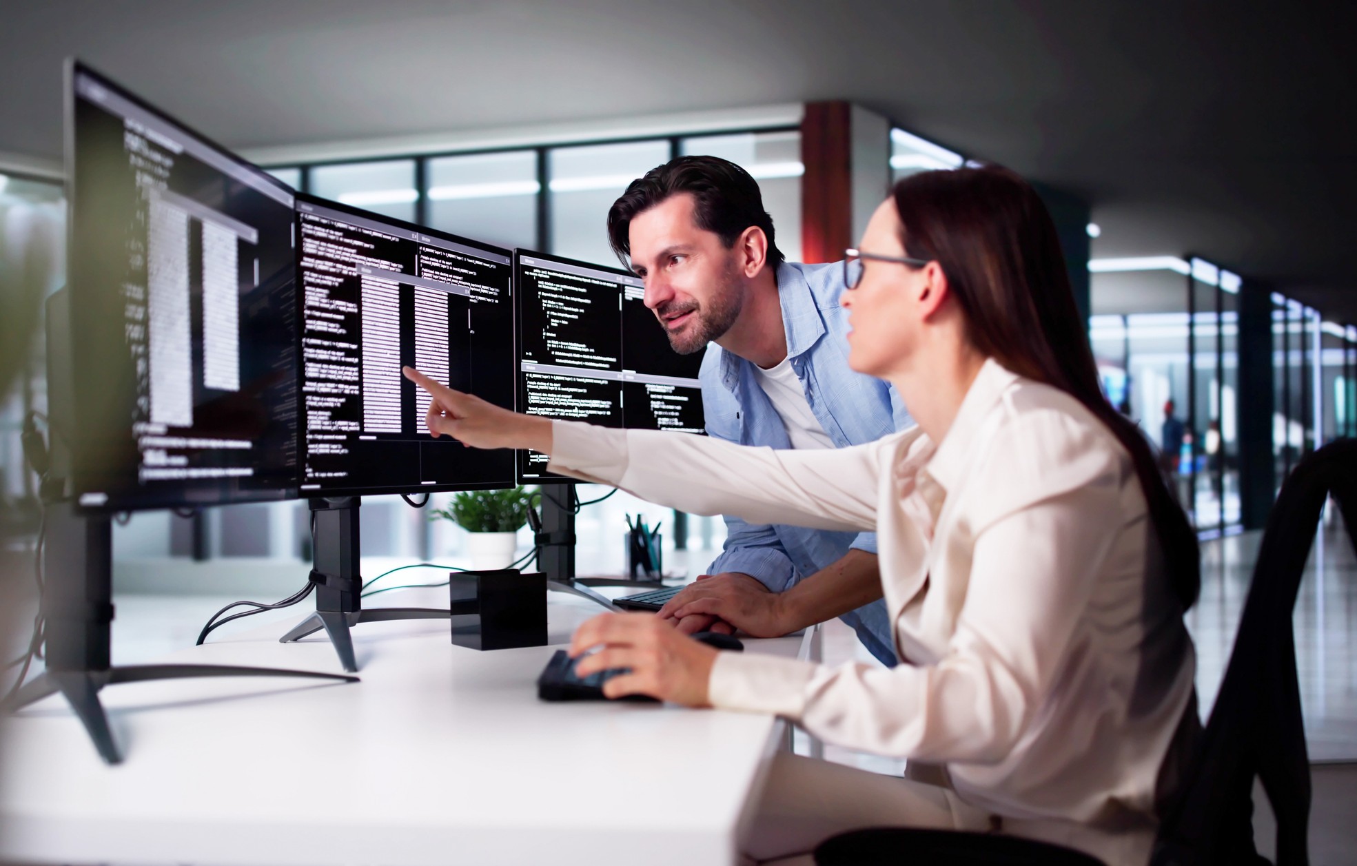 To personer samarbeider foran flere skjermer