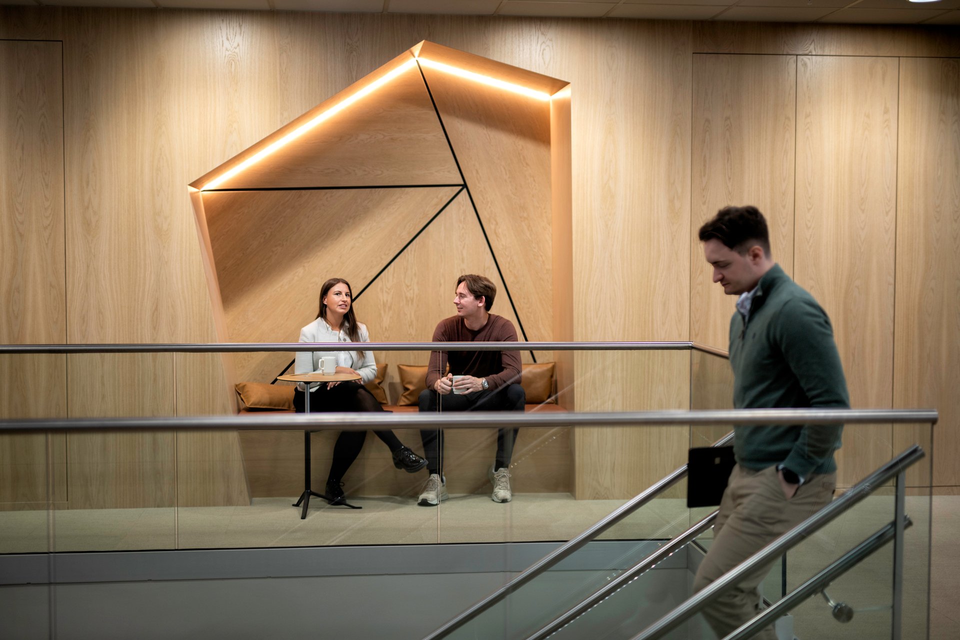 A male employee leaves his job down a flight of stairs with a non-competition clause. Two colleagues are sitting in a relaxed office space in the background.