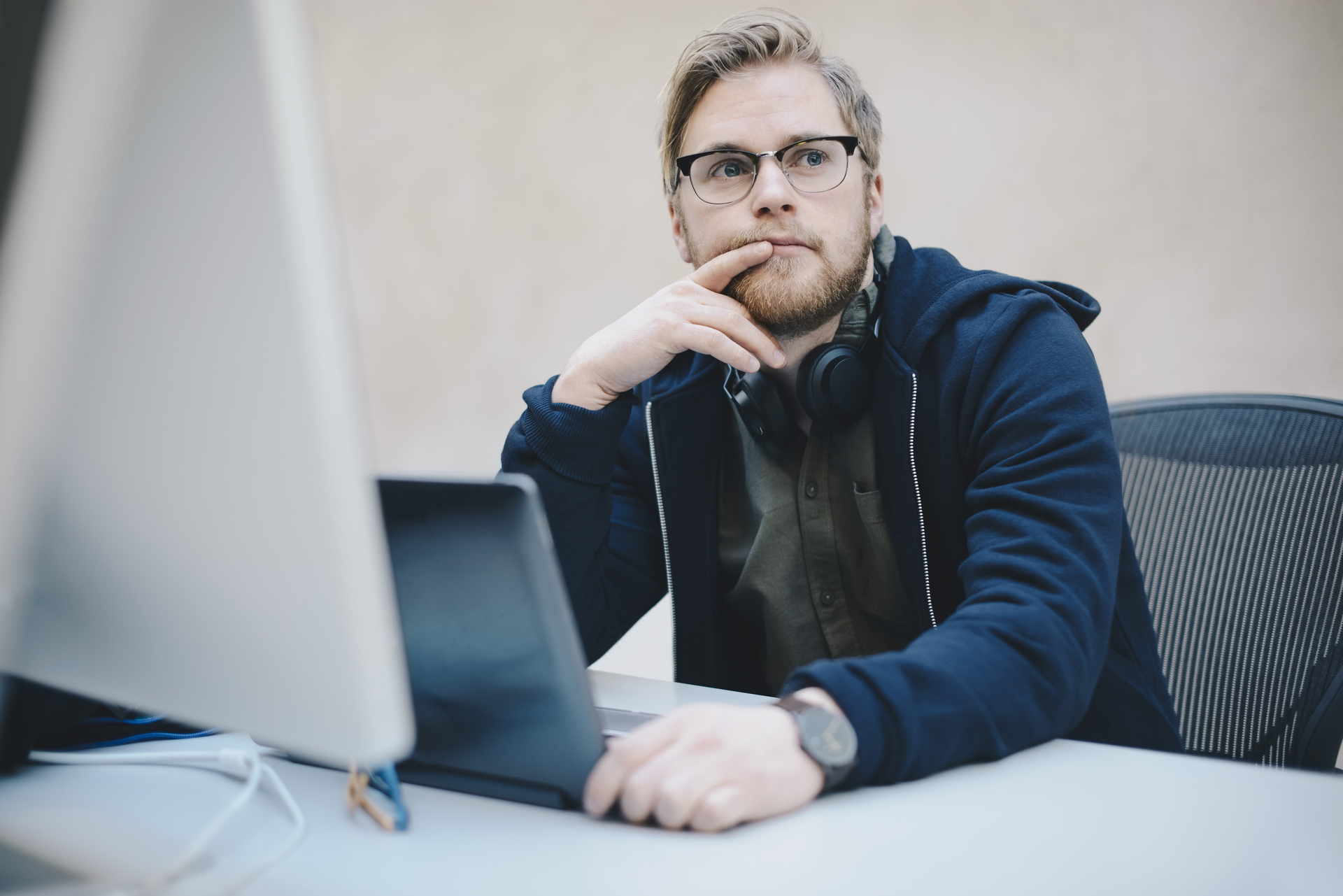 Young man sits in front of a laptop in a green sweater and looks questioningly into the air