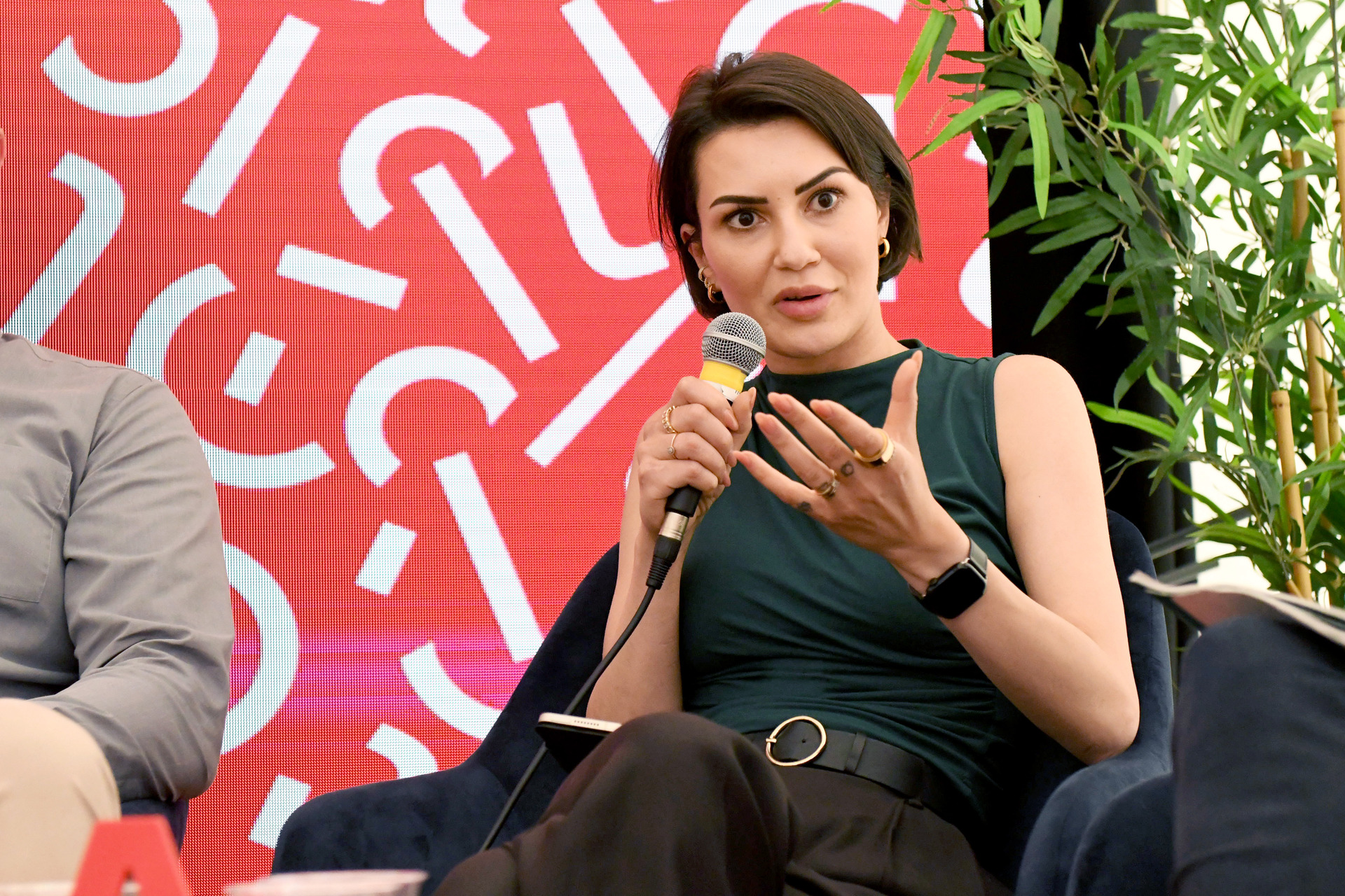 Woman sits in a chair on a stage with microphone in hand.
