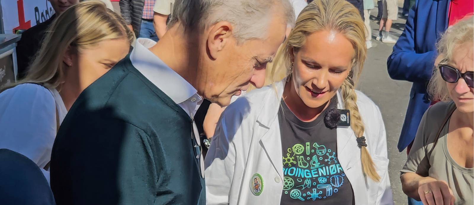 Statsminister Jonas Gahr St&oslash;re st&aring;r sammen med flere personer utend&oslash;rs, blant annet en kvinne i hvit frakk og en sort t-skjorte med teksten "Bioingeni&oslash;r"