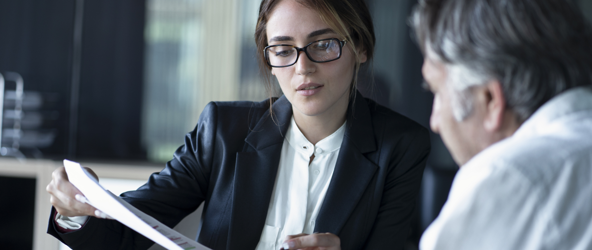 A woman and a man are sitting in an office environment discussing a document