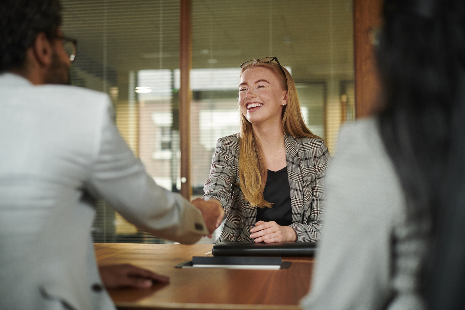 A young woman smiles and shakes hands during a job interview, symbolizing new opportunities and the importance of good employment conditions secured through collective agreements.