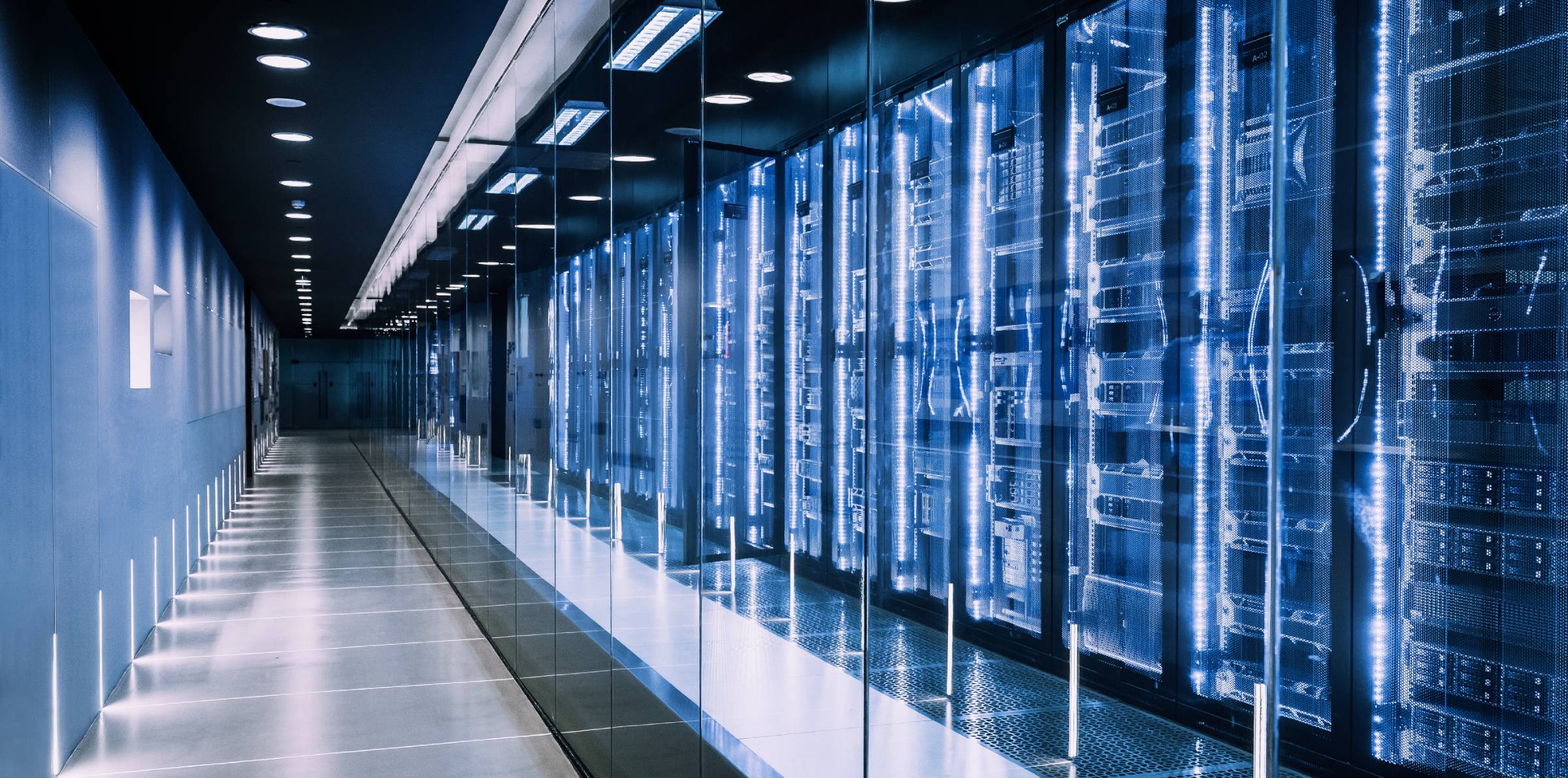 A long, futuristic corridor with glass walls showing rows of blue-glowing server racks in a row.
