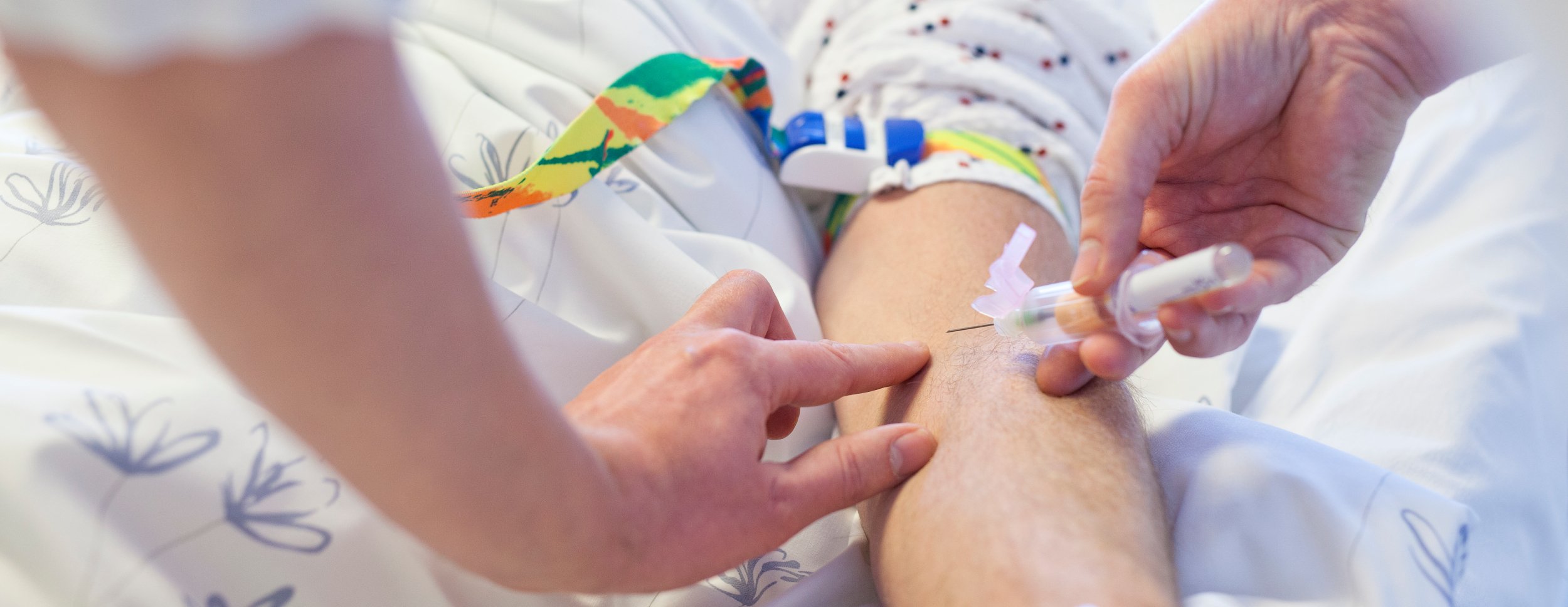 The picture shows a healthcare worker taking a blood sample by inserting a needle into a patient's arm.