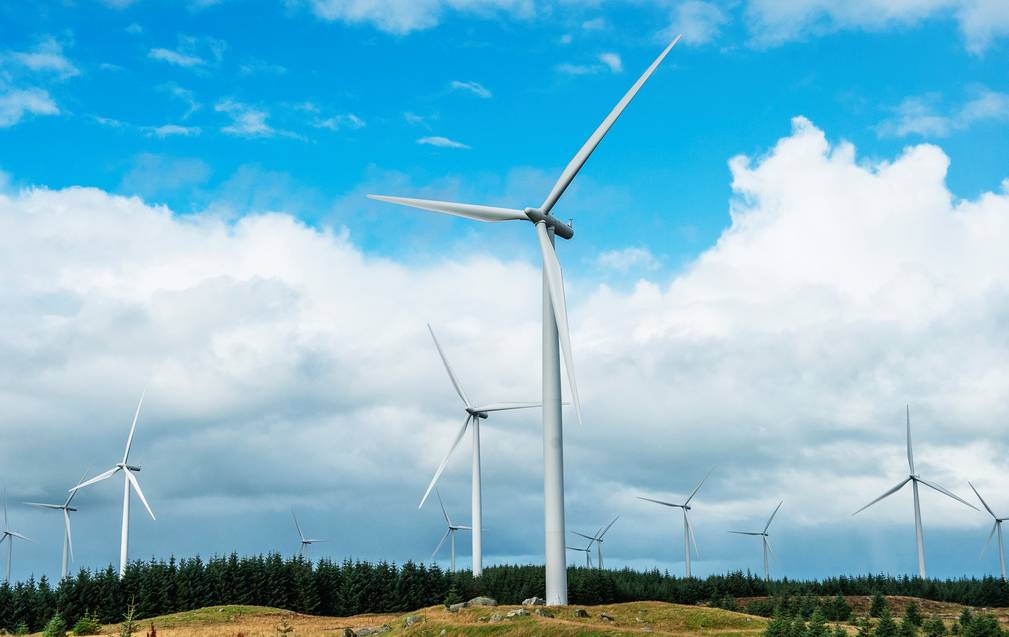 Bilde av et landskap med vindmøller. I bakgrunnen er det blå himmel og skyer.