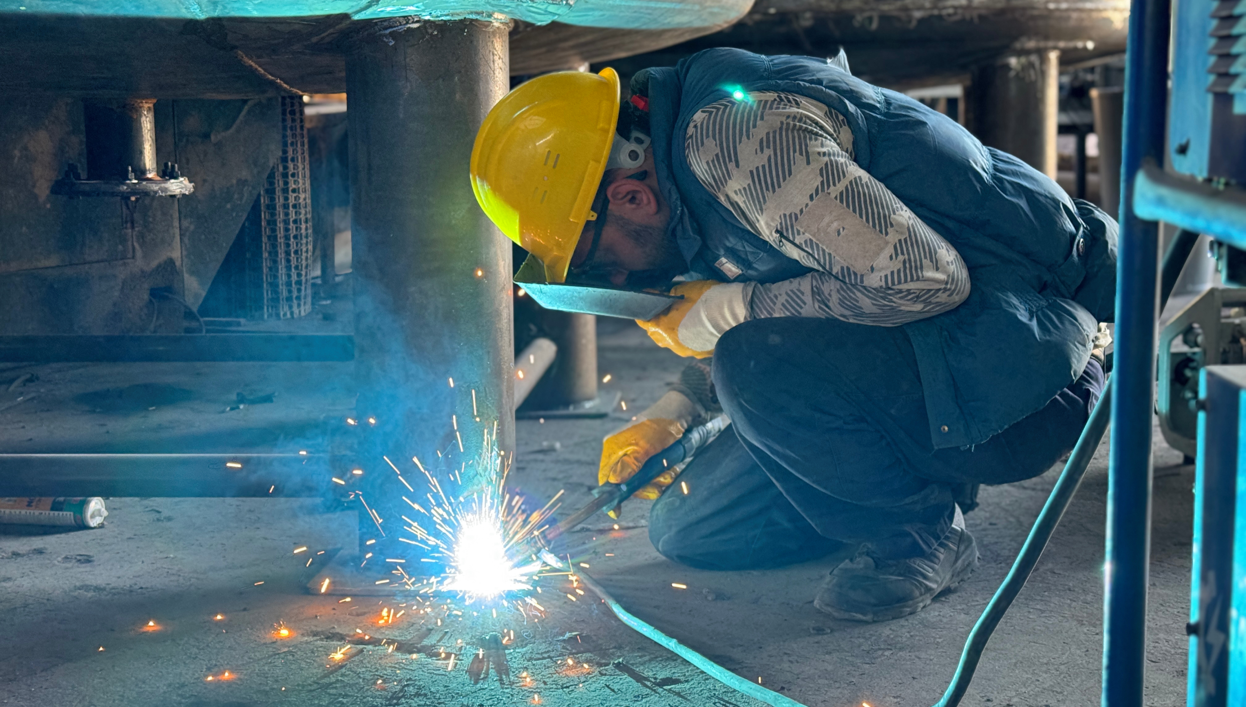 En arbeider med hjelm og vernebriller som sveiser.