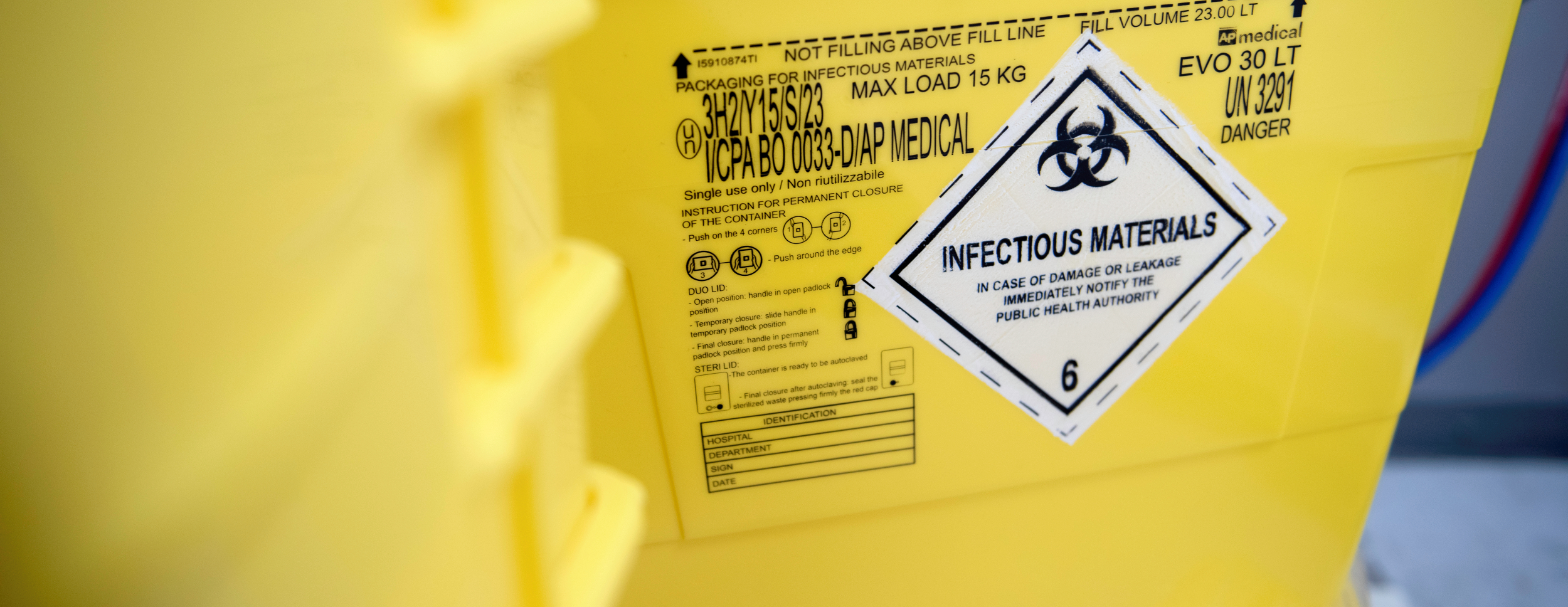 Bildeutsnitt av en gul plastbeholder med fokus på advarselsmerket for smittefarlig avfall.