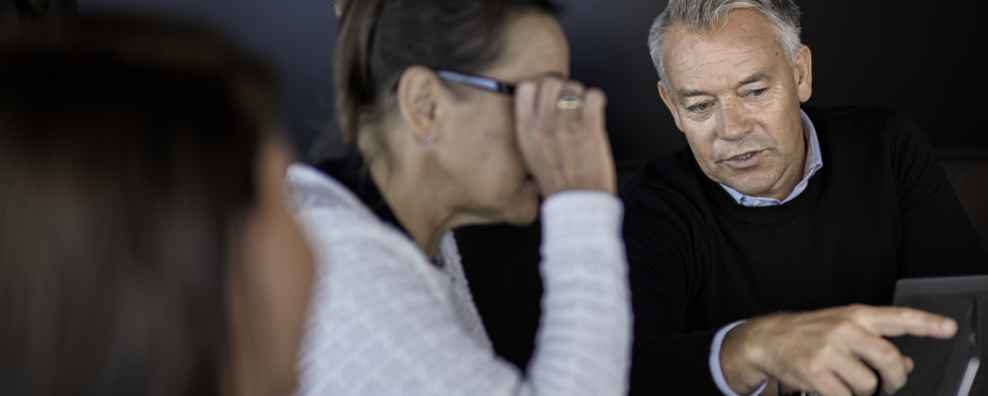 Three people discussing, one person pointing at a laptop screen.