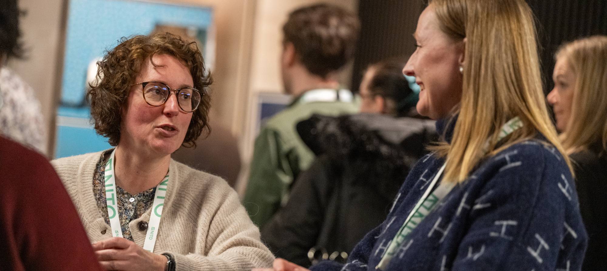 To kvinnelige deltakere på NITOs tariffkonferanse i samtale med hverandre. Mennesker i bakgrunnen.