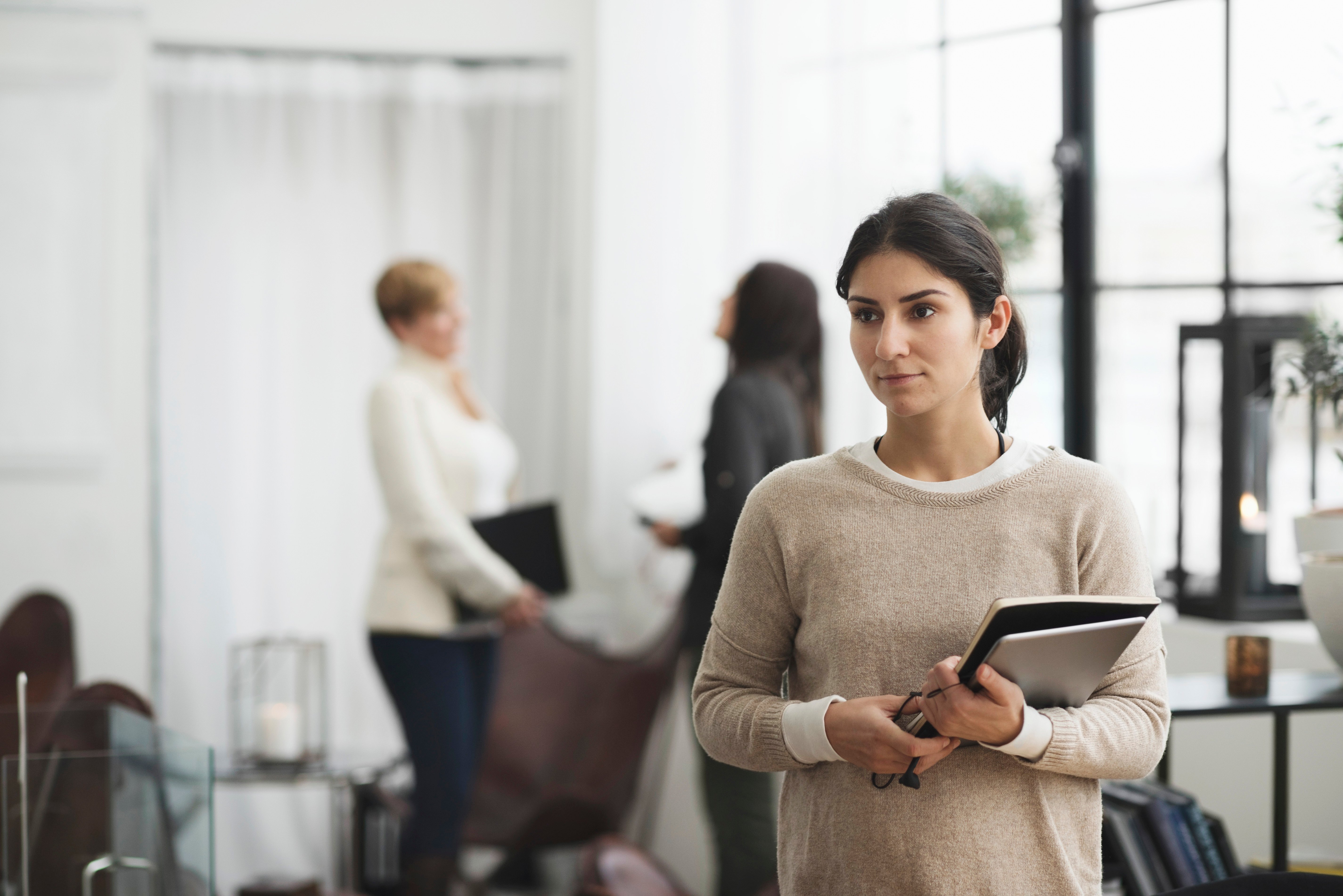 A woman with a serious expression holds a tablet in an office environment. Symbolizes the courage and seriousness of reporting censurable conditions in the workplace.