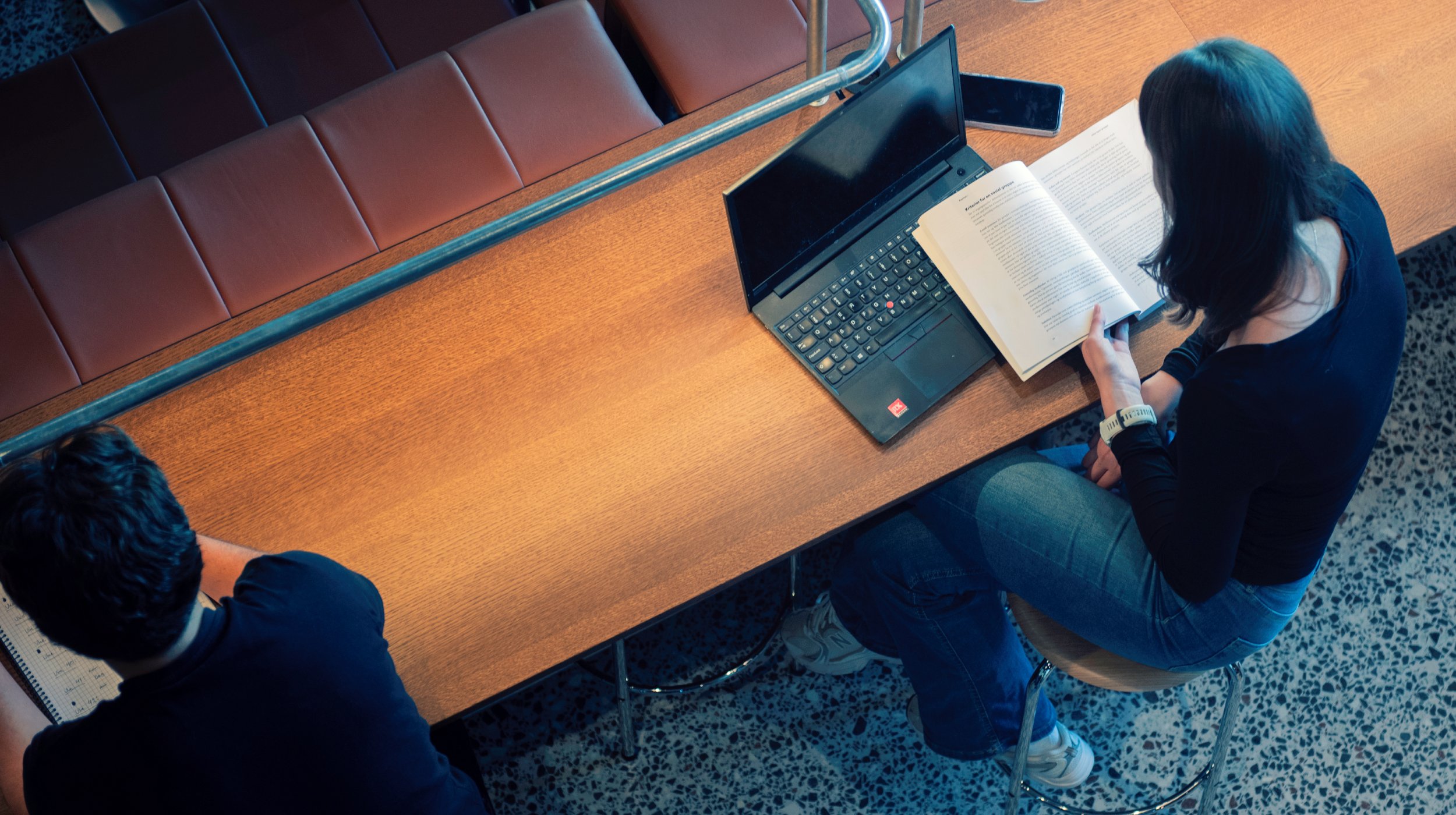 Student sitting with laptop, book and phone in a reading room