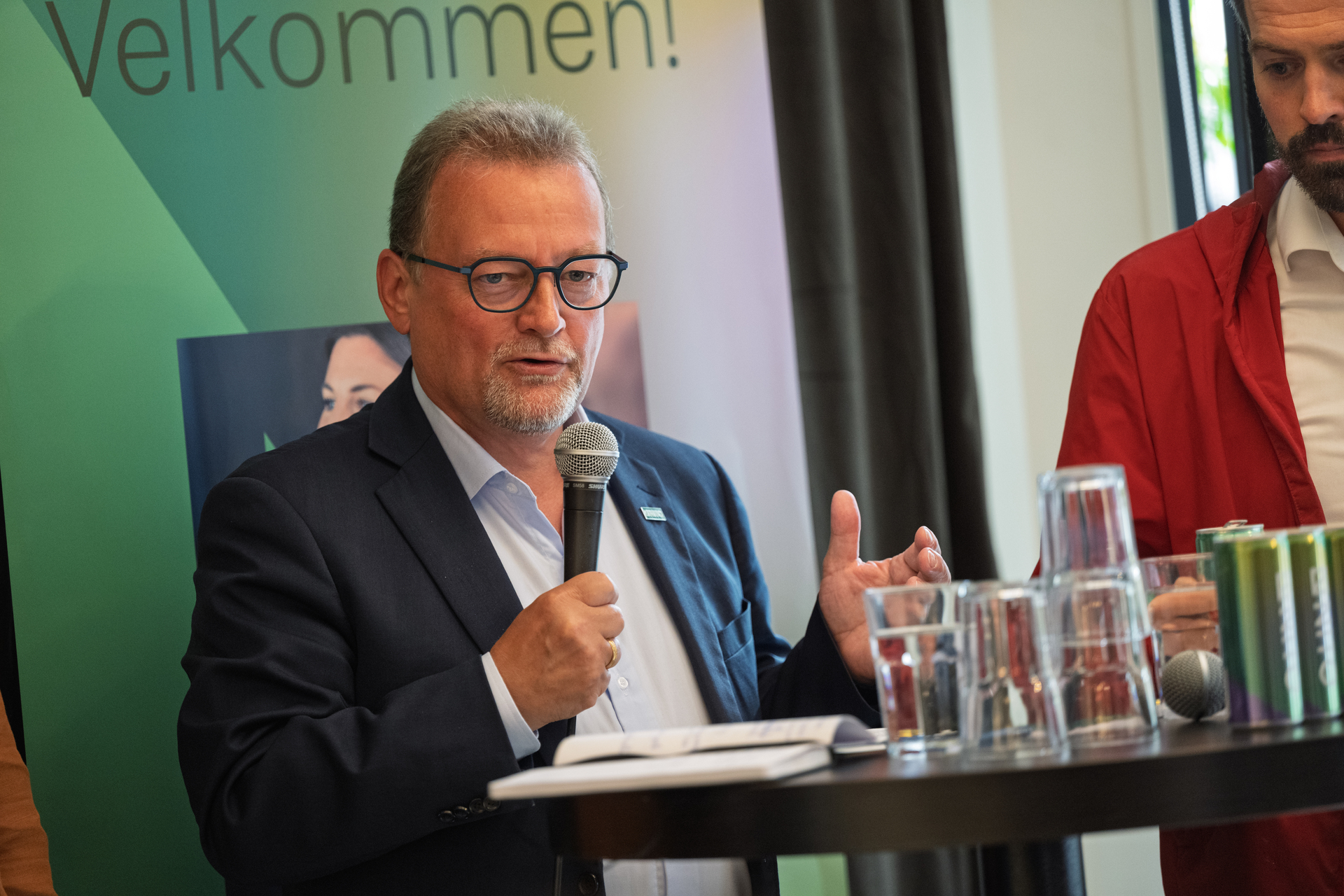 Mann med briller står med mikrofon i hånda