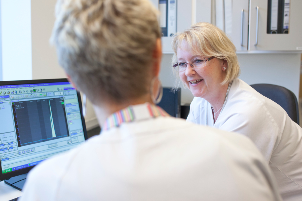 Bildet viser to bioingeniører i hvite frakker ved en dataskjerm. Den ene smiler og ser på den andre, som jobber ved skjermen.