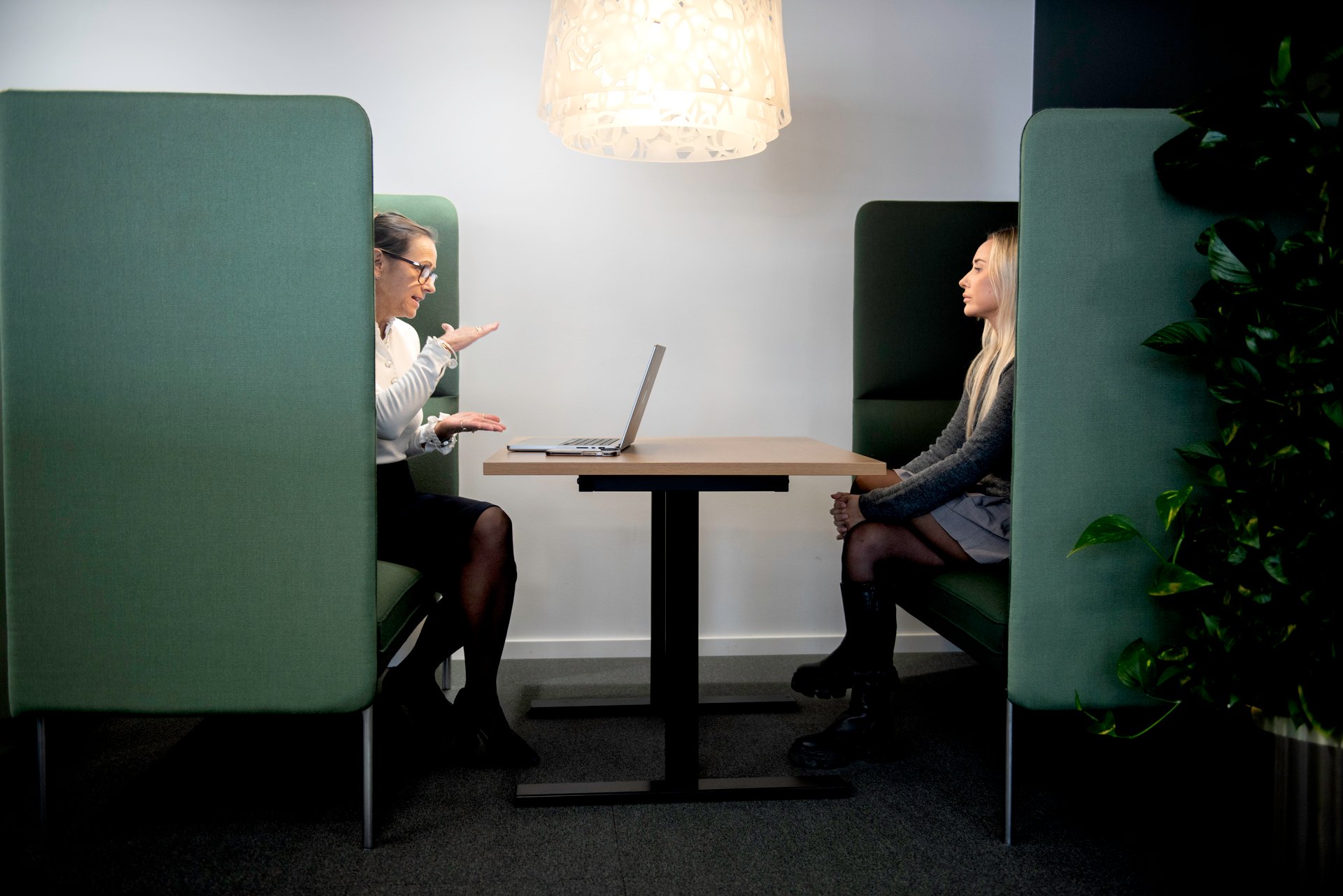 Two ladies are sitting in an open-plan office facing each other.
