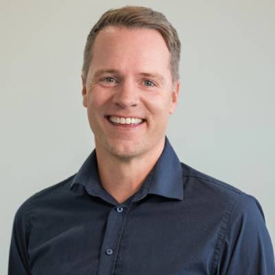 Man in dark blue shirt with short, brown hair. The background is light and neutral.