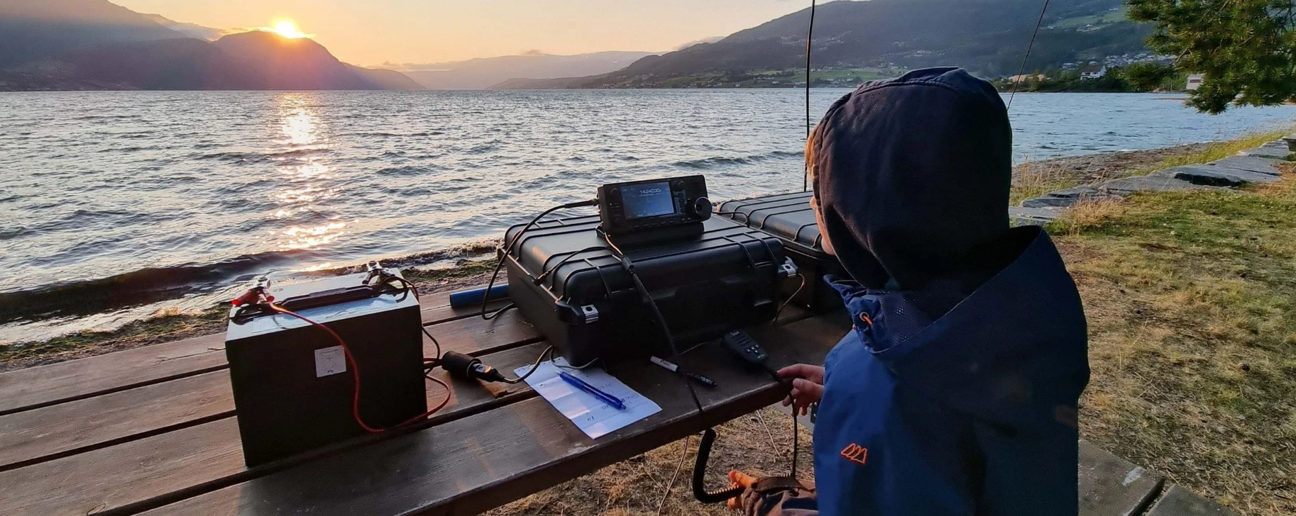 Gutt med en HF radio, foran en innsjø i solnedgang