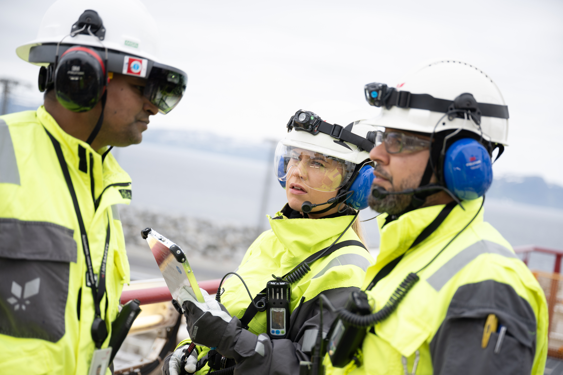 A group of engineers, wearing protective gear, discussing on a construction site. Illustrates a situation where hired workers are used.