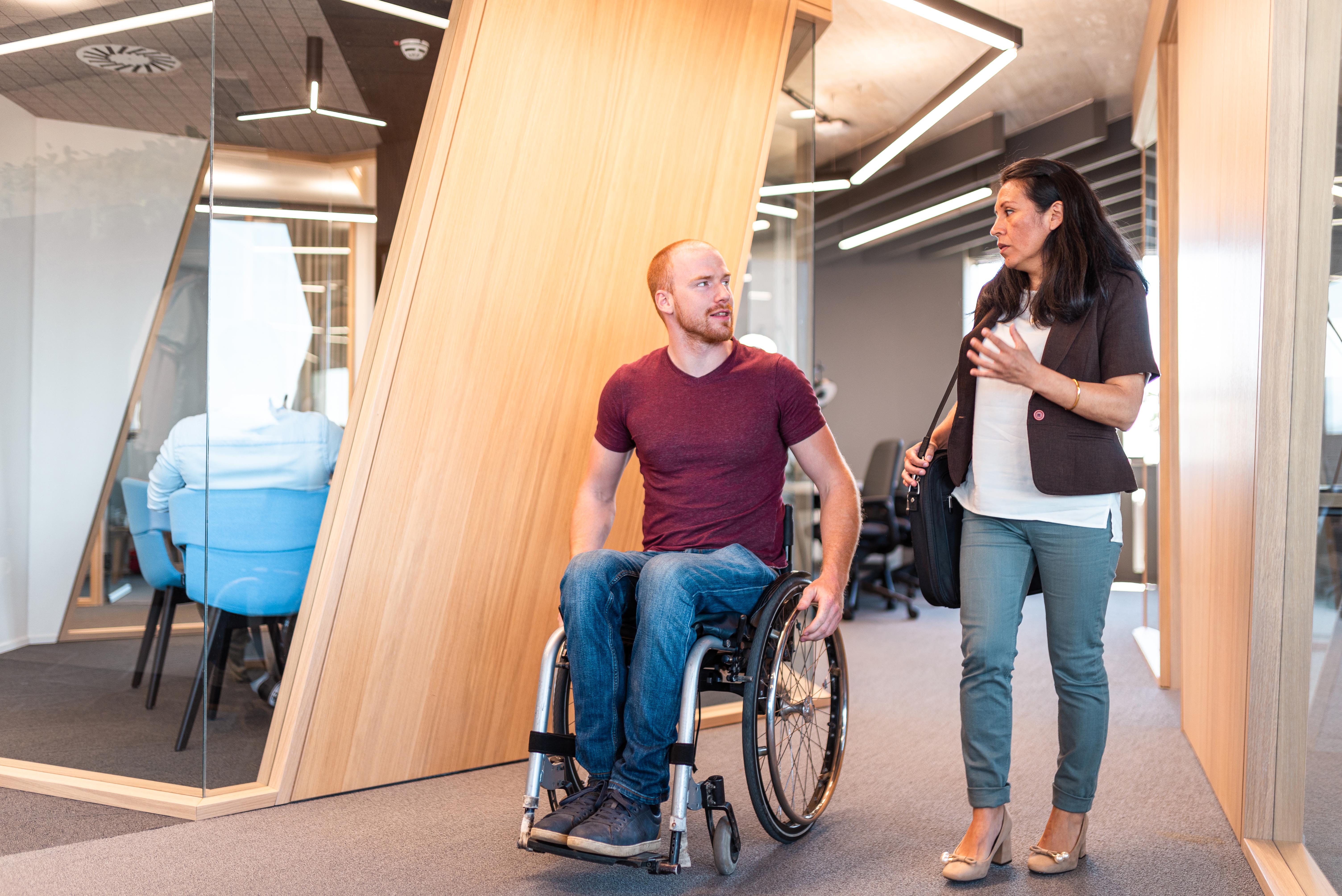 Two colleagues, one in a wheelchair, are having a conversation in the hallway at the workplace. Photo: gettyImages