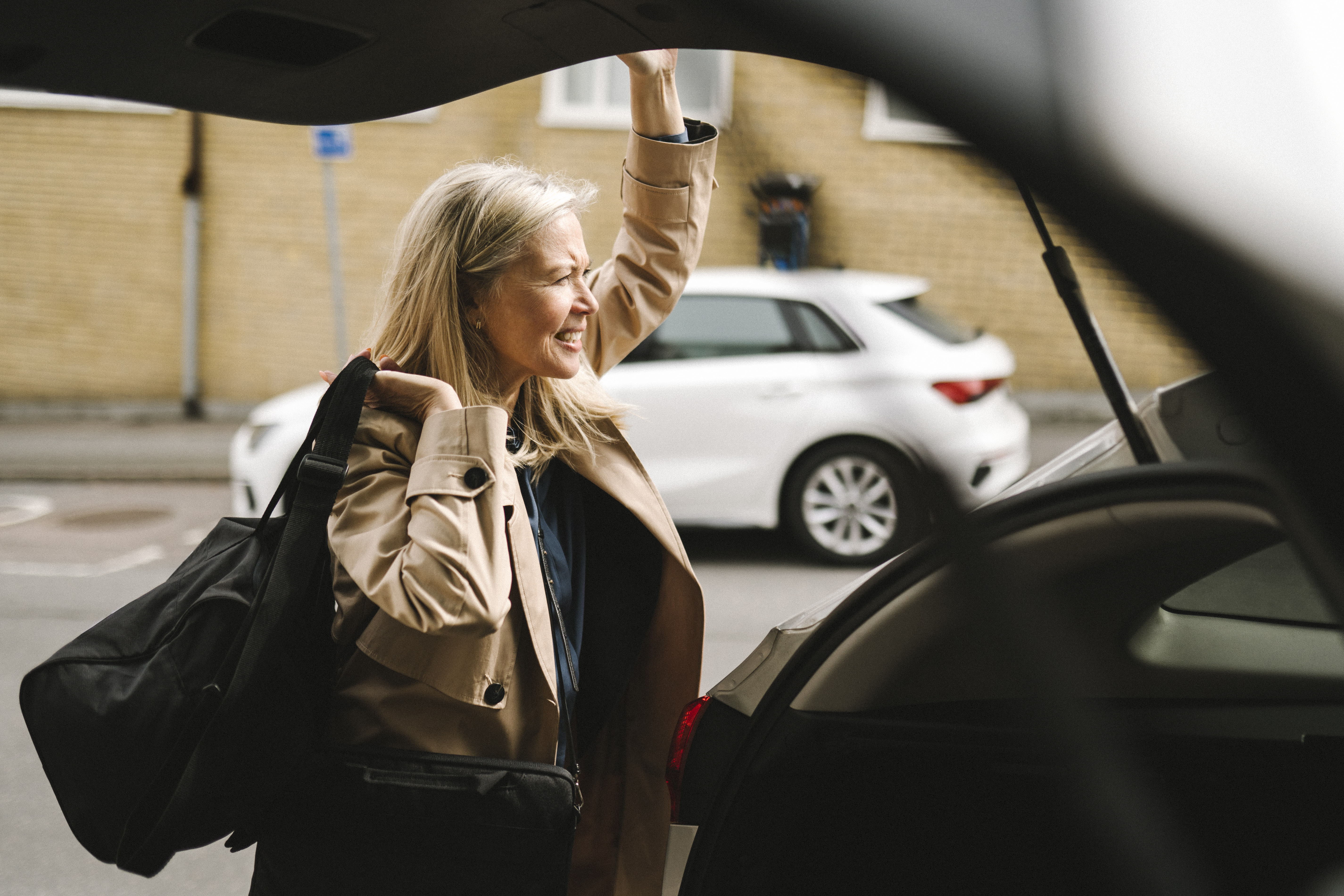 Woman with bag over shoulder closes trunk of car on way to work trip Photo: GettyImages