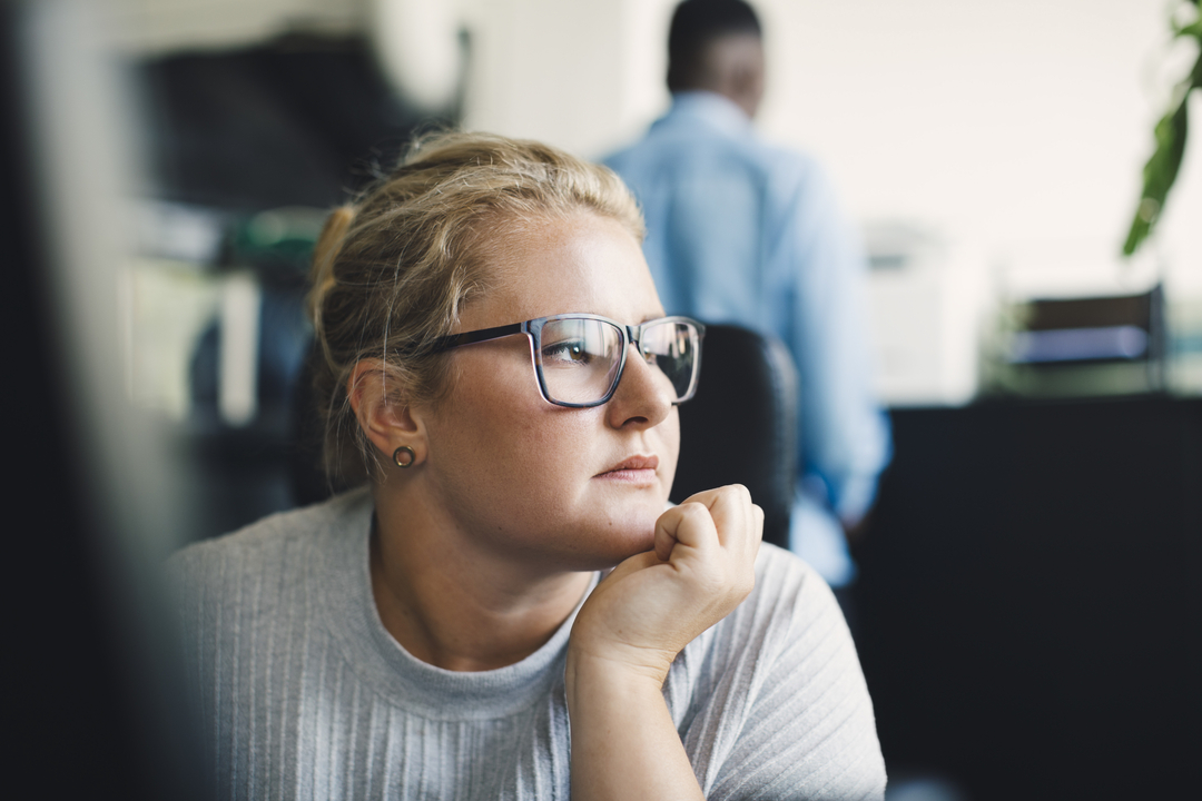 Woman with glasses thinks with her hand on her chin.