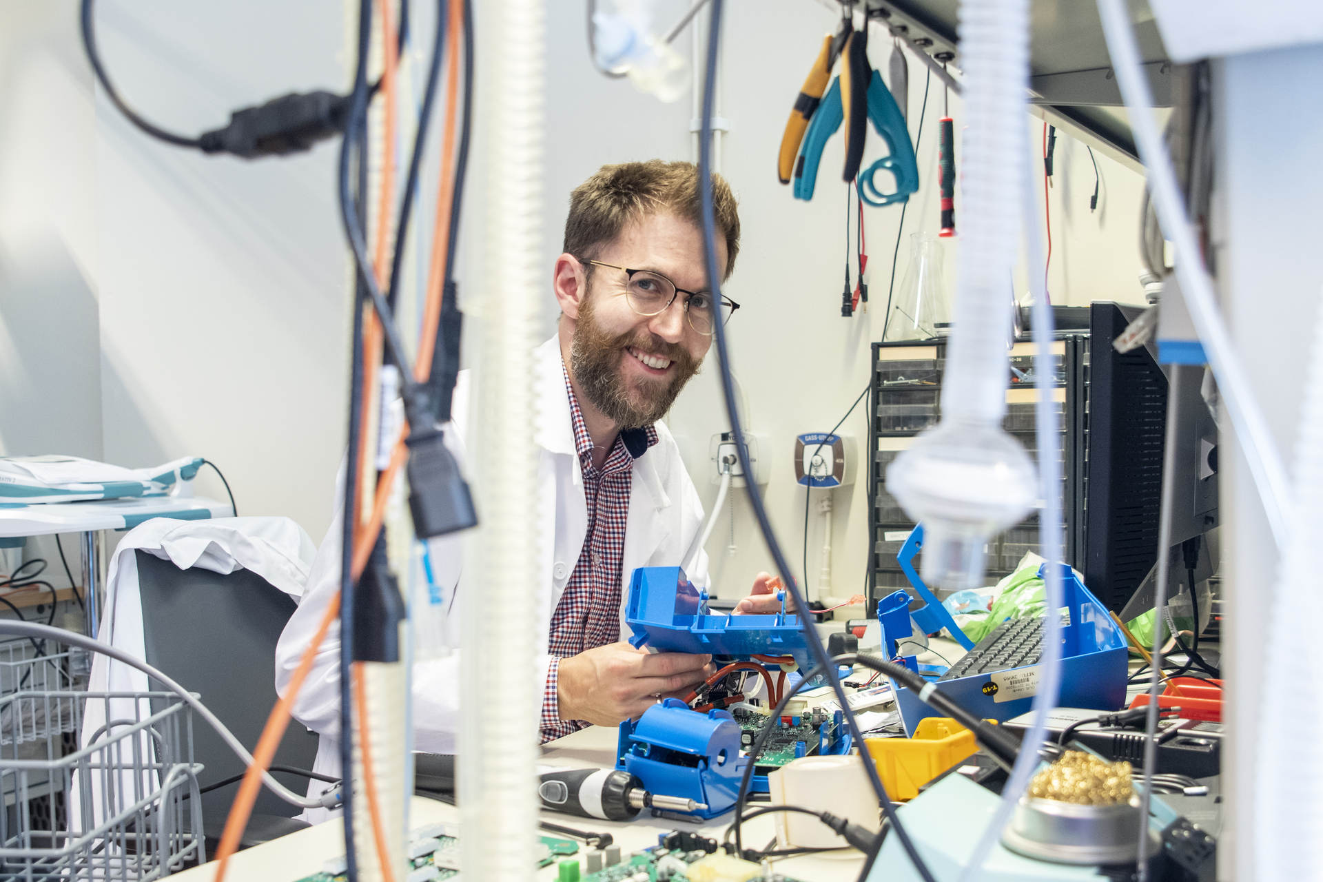 A smiling engineer in a white coat works on electronic components in a laboratory. The picture illustrates a skilled worker in a technical sector, who may be covered by a collective agreement.