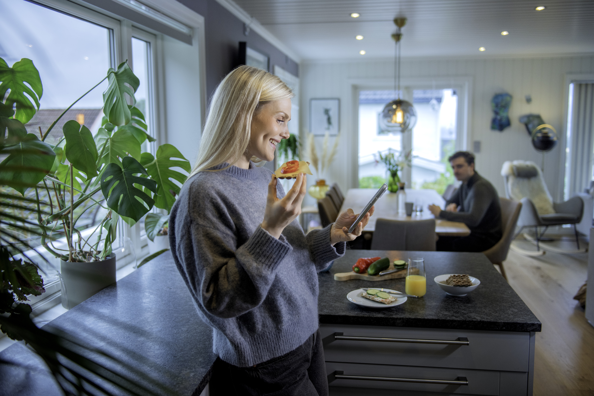 Young lady is at home looking at her phone while she eats