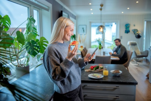 Young lady is at home looking at her phone while she eats