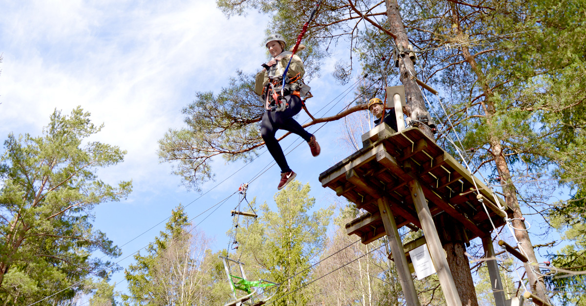 A lady hanging out in a zipline, surrounded by green trees and a blue sky.