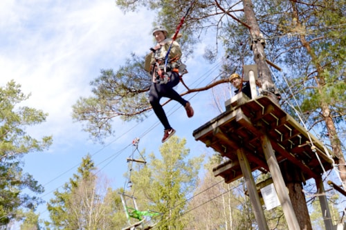 A lady hanging out in a zipline, surrounded by green trees and a blue sky.