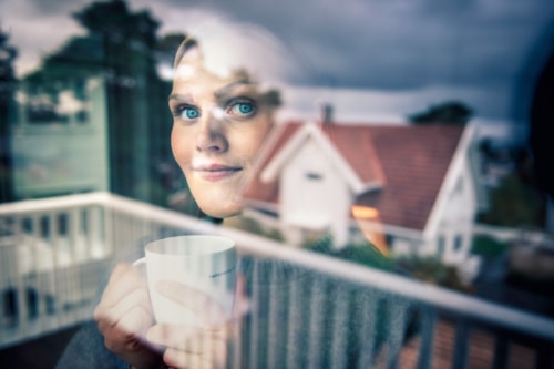 Lady looking out window, a house reflected in the window