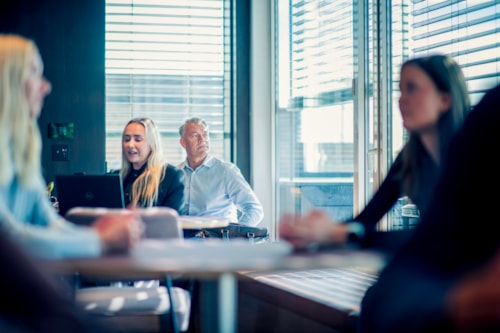 Man in open-plan office looking out of the window with several people around him