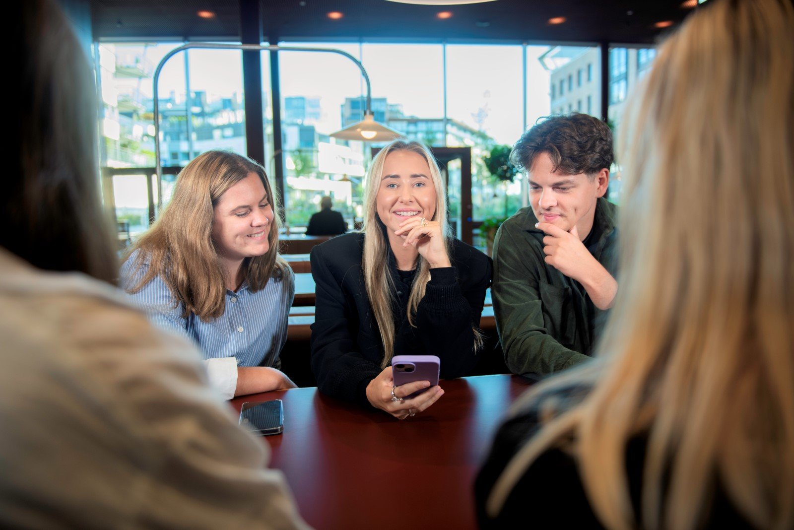 Three people are looking at a mobile phone. Photo: Luca Kleve-Ruud