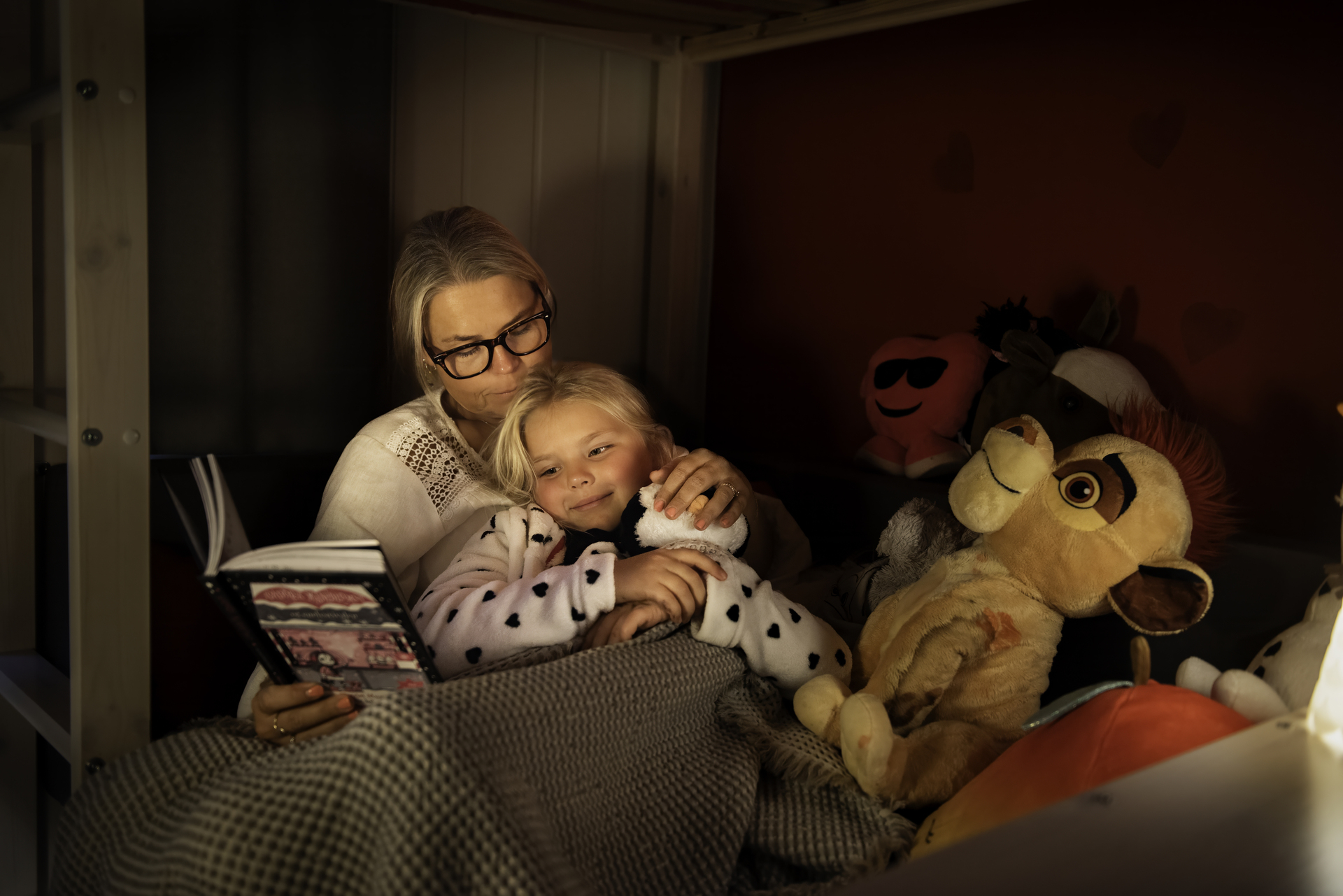 Mother and young daughter sitting in bed reading a book