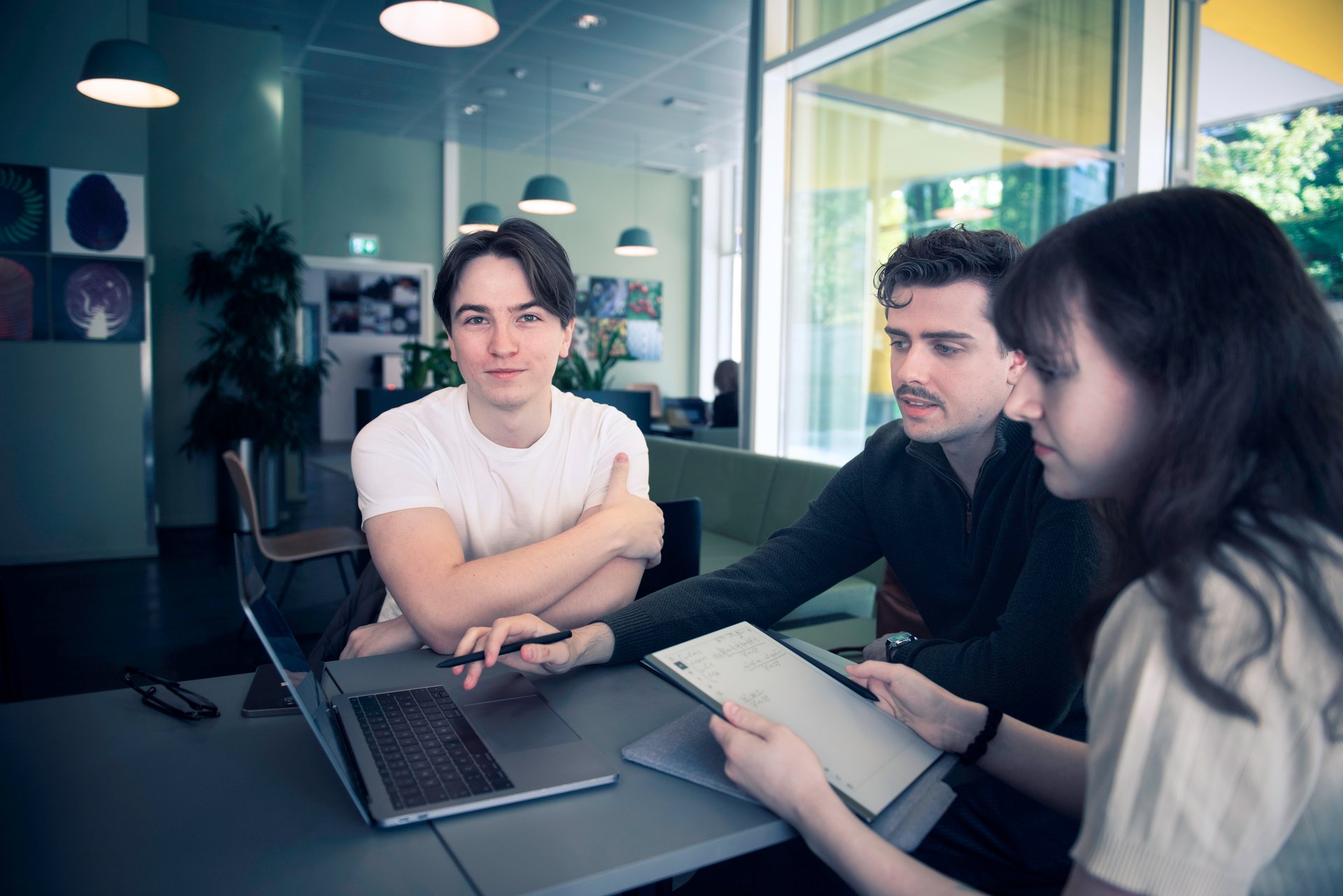 Three young engineers discuss salary and careers around a table in a modern office environment.