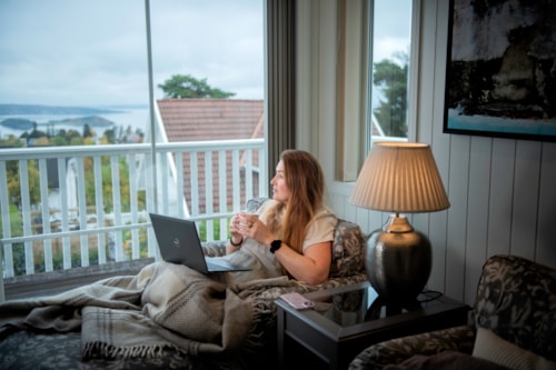 Lady sits on the sofa and looks out the window with a computer on her lap